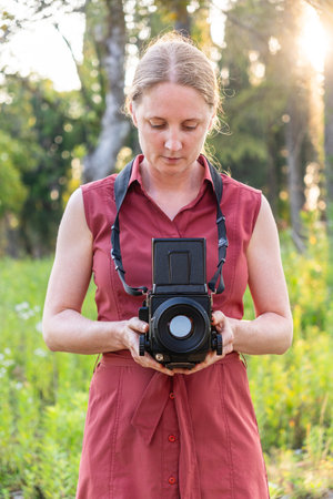 A beautiful young stylish woman photographs in nature with a retro film camera, Holiday lifestyle trip. Photographer taking picturesの写真素材