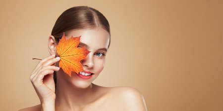 Portrait of beautiful young woman with autumn leafs. Healthy clean fresh skin natural make up beauty eyesの写真素材