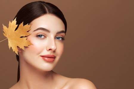 Portrait of beautiful young woman with autumn leafs. Healthy clean fresh skin natural make up beauty eyesの写真素材