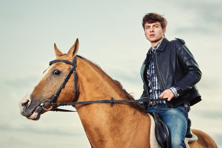 Young man in a leather jacket riding a horse outdoorsの写真素材