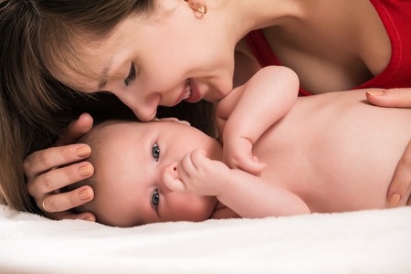 Closeup portrait of cheerful young mother with adorable newborn baby having fun at home, child care, happy parenthood, love conceptの写真素材
