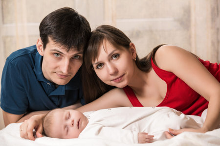 Smiling young couple and a little baby sleep in bed at home