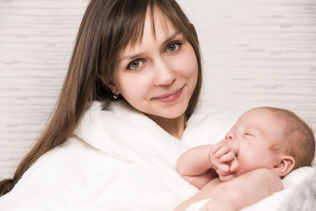 Closeup portrait of cheerful young mother with adorable newborn baby having fun at home, child care, happy parenthood, love conceptの写真素材