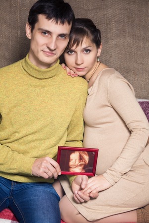Portrait of happy laughing pregnant couple showing ultrasound picture of baby, isolated on white background.の写真素材