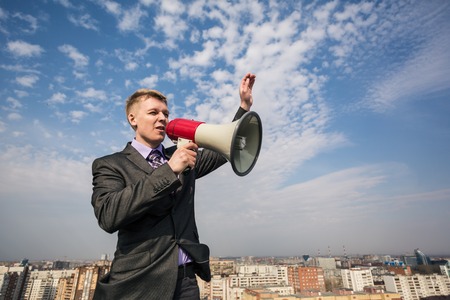 young businessman in suit screaming into megaphone on the roofの写真素材