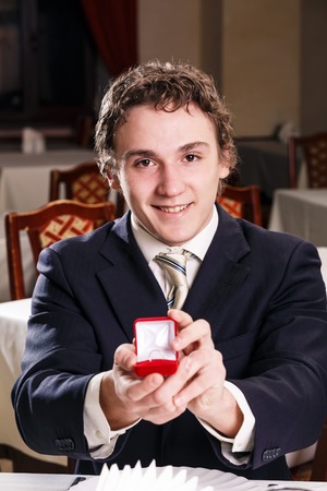 Young man presenting engagement ring in cafeの写真素材