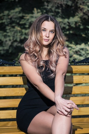 Business woman sitting on a bench, the sun shines brightly, looking straightの写真素材