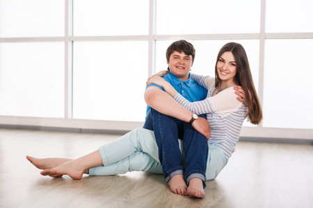 Attractive young adult couple sitting close on floor in home smiling and laughing の写真素材