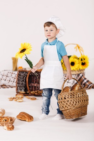 Little boy chef stands wih a basket and flower in his white chefs uniformの写真素材