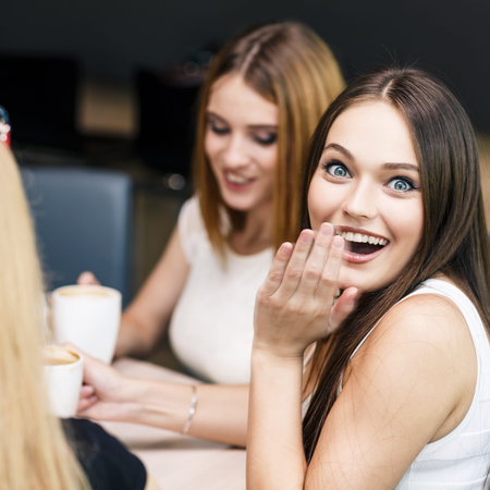 Happy women holding coffee cup while looking at each other in cafe