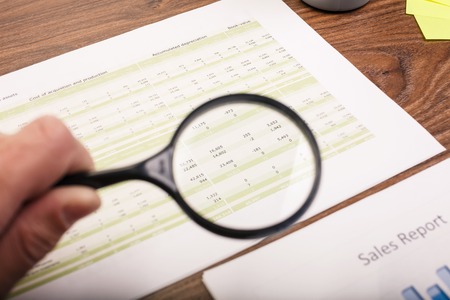 Businessman checking a graph with a magnifying glass, closeupの写真素材