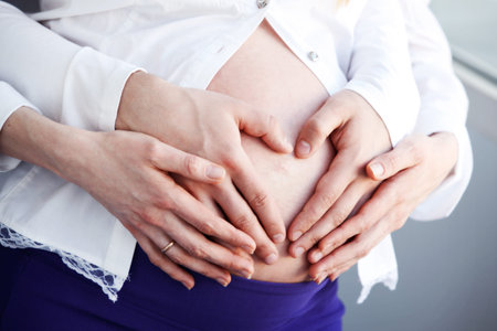 Heart shaped hands of pregnant woman and her husband