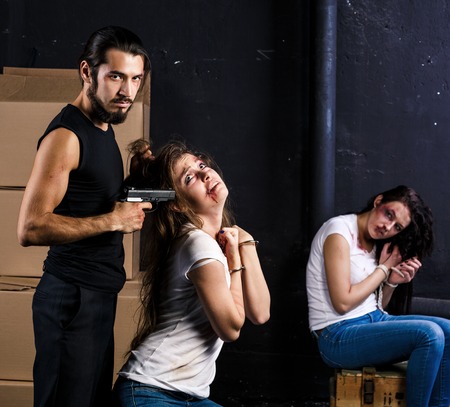 Crime. Two beautiful girls in the Business clothing kidnapped by criminals. Terrorist is threatening hostages with a gun.の写真素材