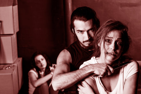 Crime. Two beautiful girls in the Business clothing kidnapped by criminals. Terrorist is threatening hostages with a knifeの写真素材