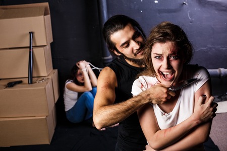 Crime. Two beautiful girls in the Business clothing kidnapped by criminals. Terrorist is threatening hostages with a knifeの写真素材