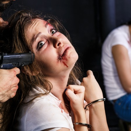 Crime. Two beautiful girls in the Business clothing kidnapped by criminals. Terrorist is threatening hostages with a gun.の写真素材