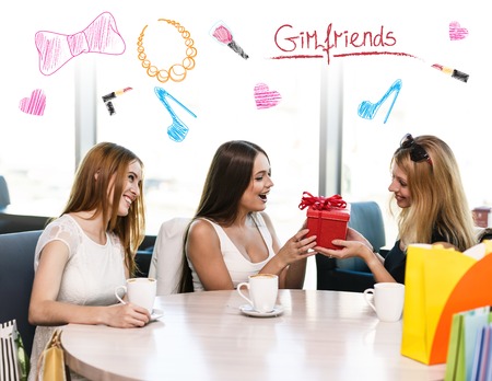Cheerful young woman surprising friend with a gift in cafeの写真素材