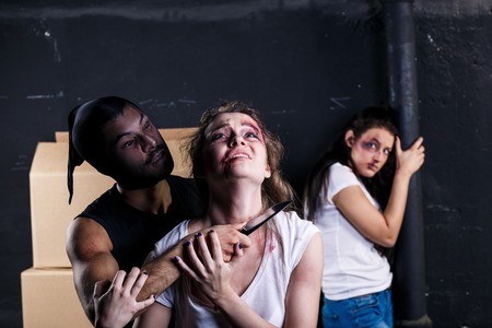 Crime. Two beautiful girls kidnapped by criminals. Terrorist is threatening hostages with a knifeの写真素材