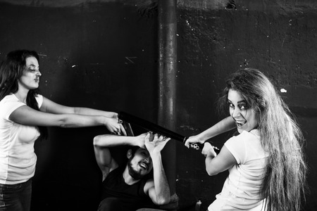 Two young women beating and shooting man on black-and-white backgroundの写真素材