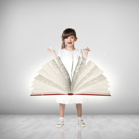 Happy cute little girl and big book in front of sheの写真素材