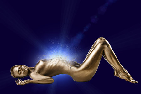woman with gold glossy skin lying down on the dark blue backgroundの写真素材