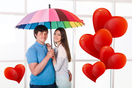 Happy smiling couple under a umbrella with big hearts in airの写真素材