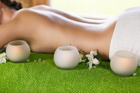 Beautiful young woman lies at the massage table with candles foregroundの写真素材