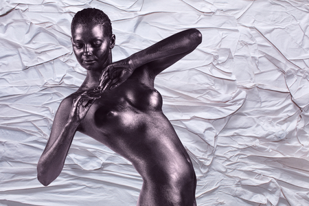 Young beautiful naked woman with glossy skin is posing on the crumpled paper backgroundの写真素材