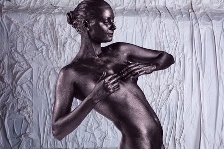 Young beautiful naked woman with glossy skin is posing on the crumpled paper backgroundの写真素材