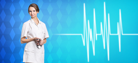 Young woman doctor stands near pulse line on the blue backgroundの写真素材