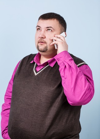 Businessman with overweight speaks on the phone on the blue backgroundの写真素材