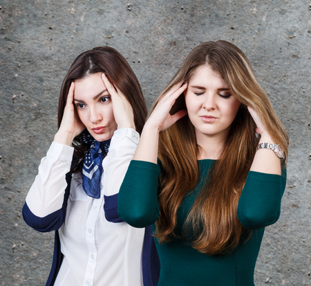 Two women with a headache on the gray wall backgroundの写真素材