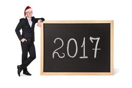 Young business woman in xmas hat stands near big chalkboard with new year date.