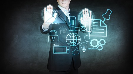 Businessman moving icons on digital virtual screen over dark gray backgroundの写真素材