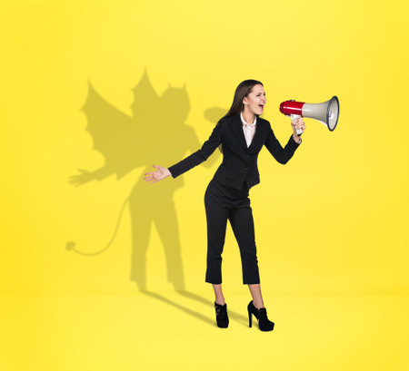 Businesswoman screams to loudspeaker with devil shadow behind the backの写真素材
