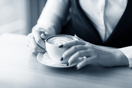 Woman holding cup of capuccino on wooden table.の写真素材