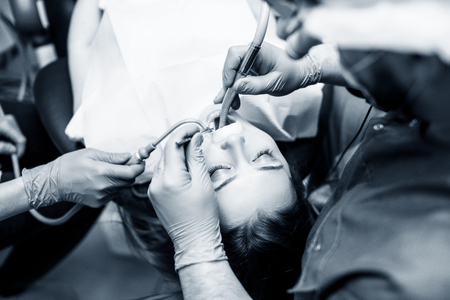 Male dentist treating teeth to young woman patient in clinic.の写真素材