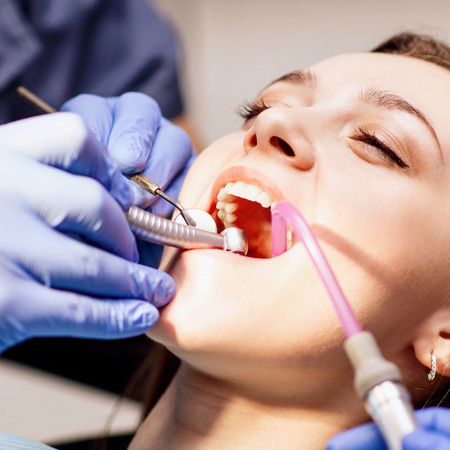 Male dentist treating teeth to young woman patient in clinic.の写真素材