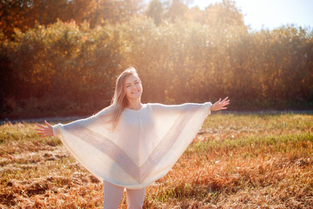 Cheerful girl with raised hands on the field in warm autumn season.の写真素材