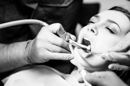 Male dentist treating teeth to young woman patient in clinic.の写真素材