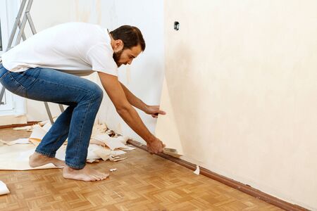 Man in with a scraper in the process of removing old wallpaper.の写真素材