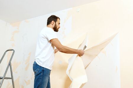 Man in with a scraper in the process of removing old wallpaper.の写真素材