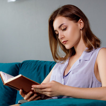 Young woman sits and relax on the couch and looks in her diary.