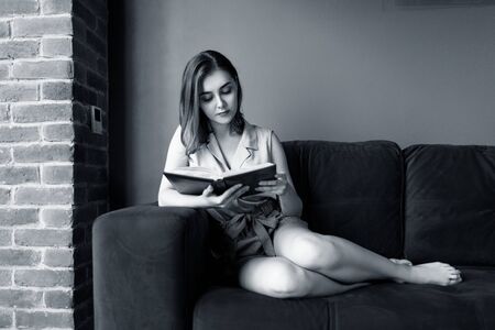 Young woman sits and relax on the couch and looks in her diary.の写真素材