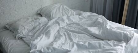 Untidy crumpled bed with white bedclothes.の写真素材