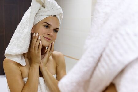 Young woman after shower looks in the mirror and admires herself.の写真素材