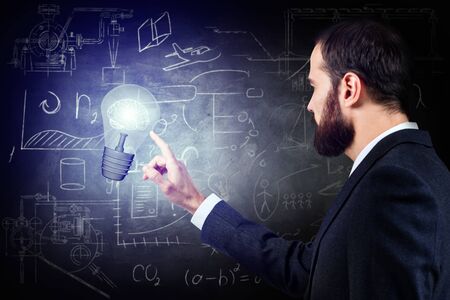 Businessman hand touches lightbulb over gray wallの写真素材