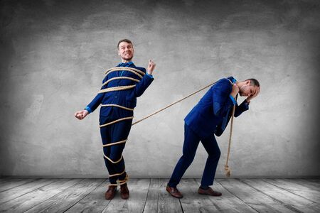 Tied businessman pulls angry himself with a rope.の写真素材