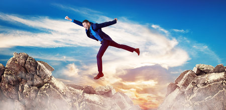 Young businessman flying through the gap among mountains. Over blue sky background