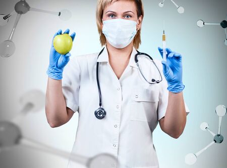 Woman doctor standing with apple and syringe among molecules.の写真素材